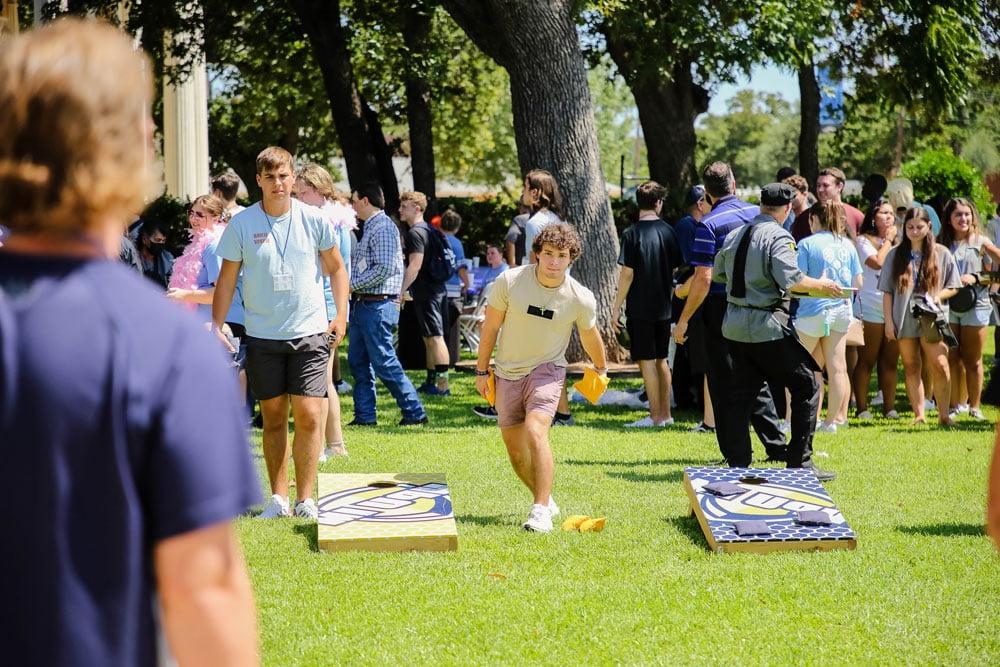 Group of Howard Payne University students participating in an outdoor cornhole game on a sunny day. | HPU
